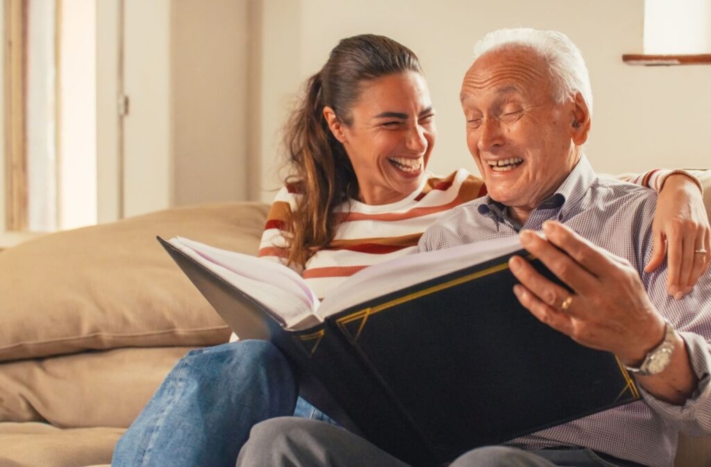 A senior and their child laugh as they look through a photo album together.