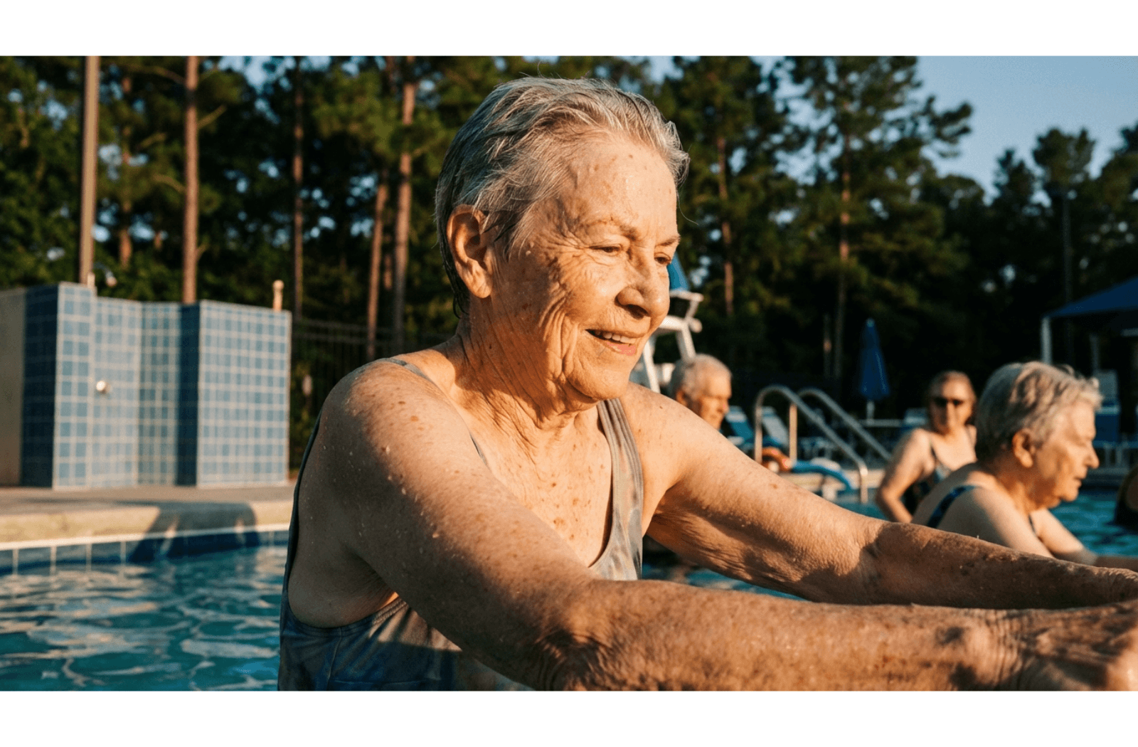 Older adult moving arms through water in a swimming pool during an exercise session, with sunlight reflecting off the water surface.